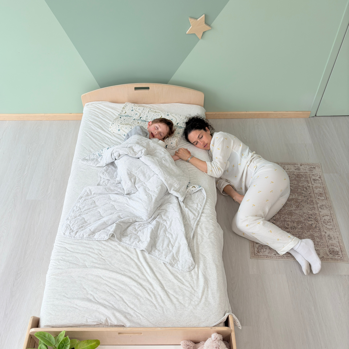 Mother sleeping beside her child on a Montessori twin floor bed made of birch wood, with cozy bedding in a serene, minimalist bedroom – shows real-life bonding and easy nighttime access for parents – ideal for gentle sleep transitions, co-sleeping alternatives, and independent sleep routines – handcrafted in Canada by Sapiens Child, available in birch or maple