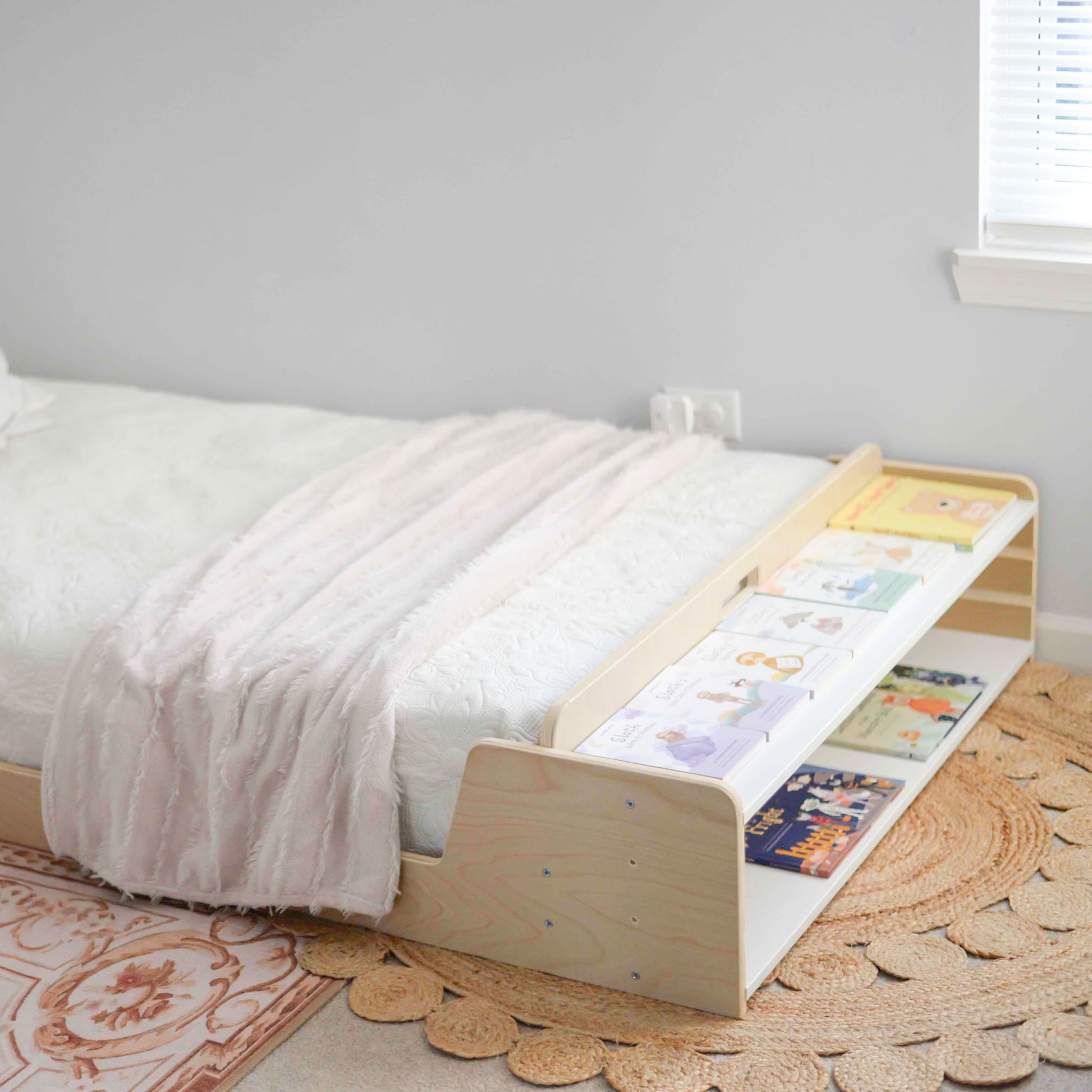 Montessori-inspired floor bed with adjustable shelves at the foot, allowing customization for storage needs. The two base levels can be set at different heights to fit books, slippers, a water cup, or decor like plants. Designed for convenience and independence, this versatile space keeps essentials within easy reach.