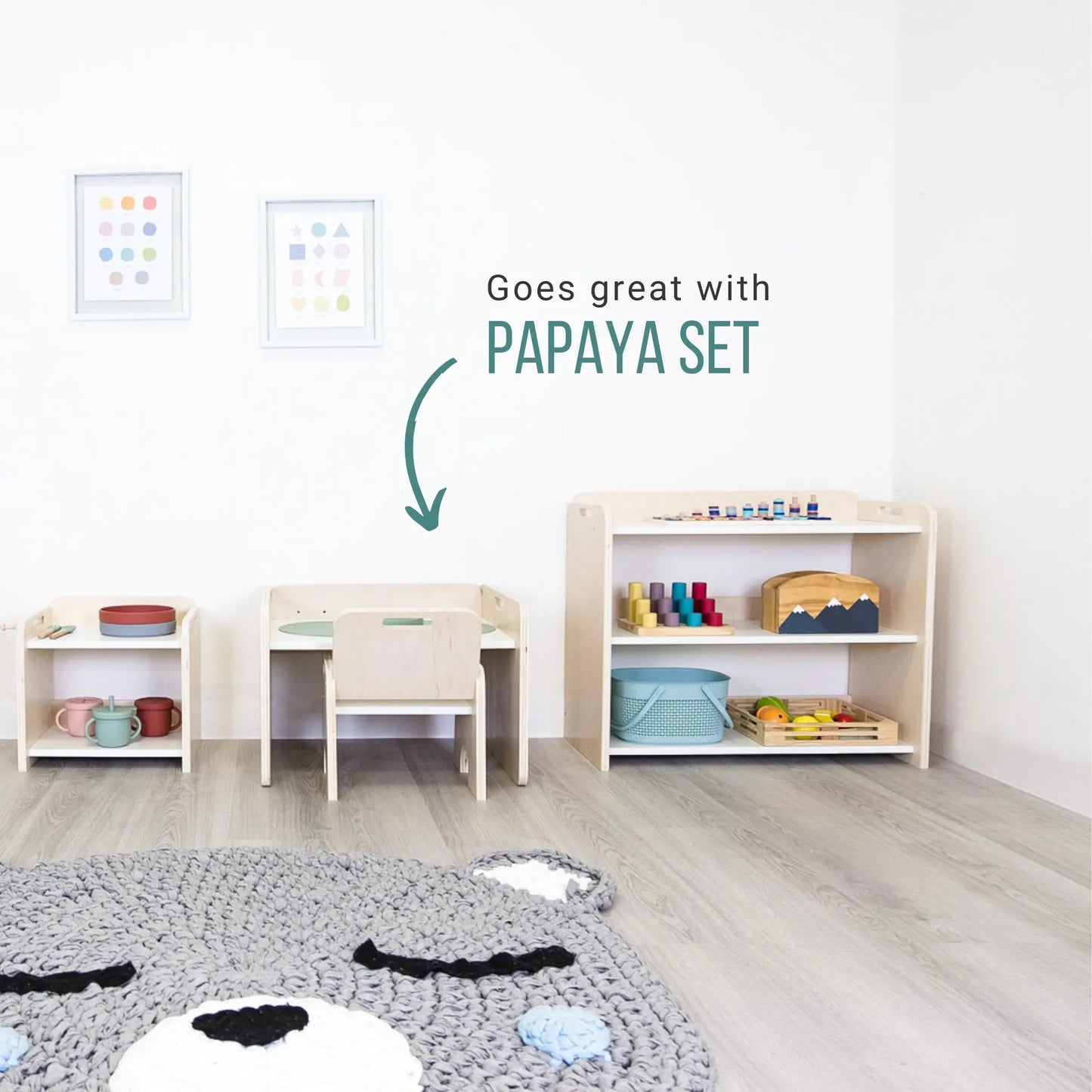 Premium Montessori shelf for toddlers, made in Canada from plywood with rounded corners. Features three accessible levels for toys and learning materials, including green storage bins on the bottom shelf, designed to encourage independence and organization in young children and a table and chair.