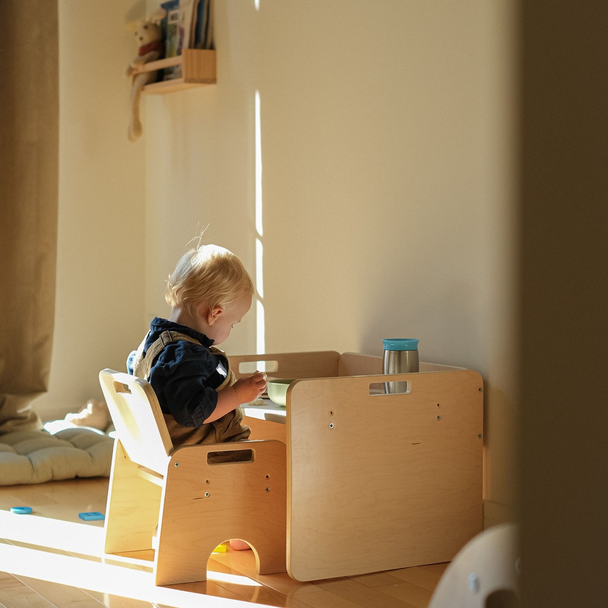 beautiful wood warm colors sunshine comming in while a toddler eats in his montessori compact table and chair set.