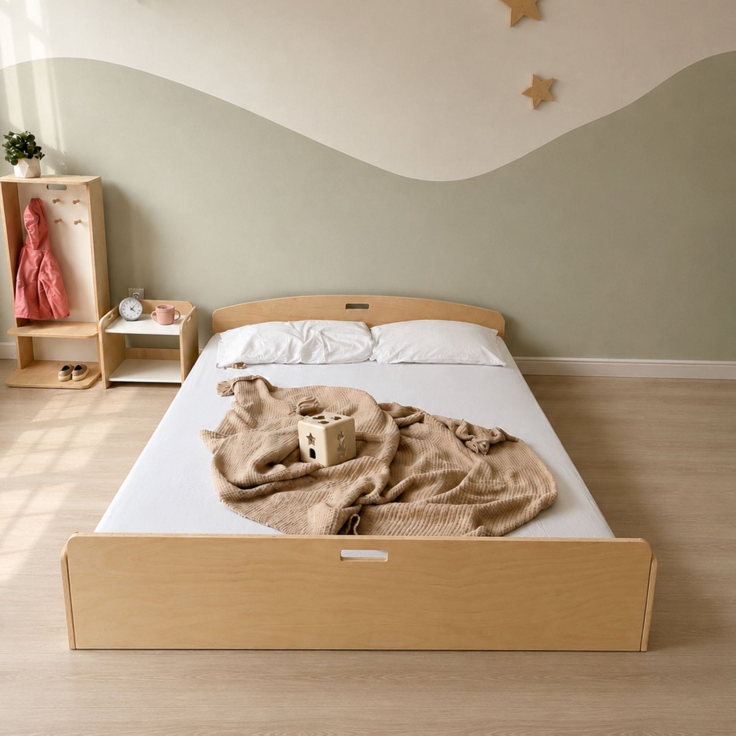A light natural wood twin-size bed frame with a matching footboard and headboard, styled in a child's bedroom with a beige blanket, white bedding, and a small wooden toy on the mattress. The background features a sage green and white wavy wall design.