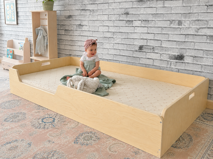 Child sitting inside a twin size floor bed from Sapiens Child with a textured wall and rug in the background