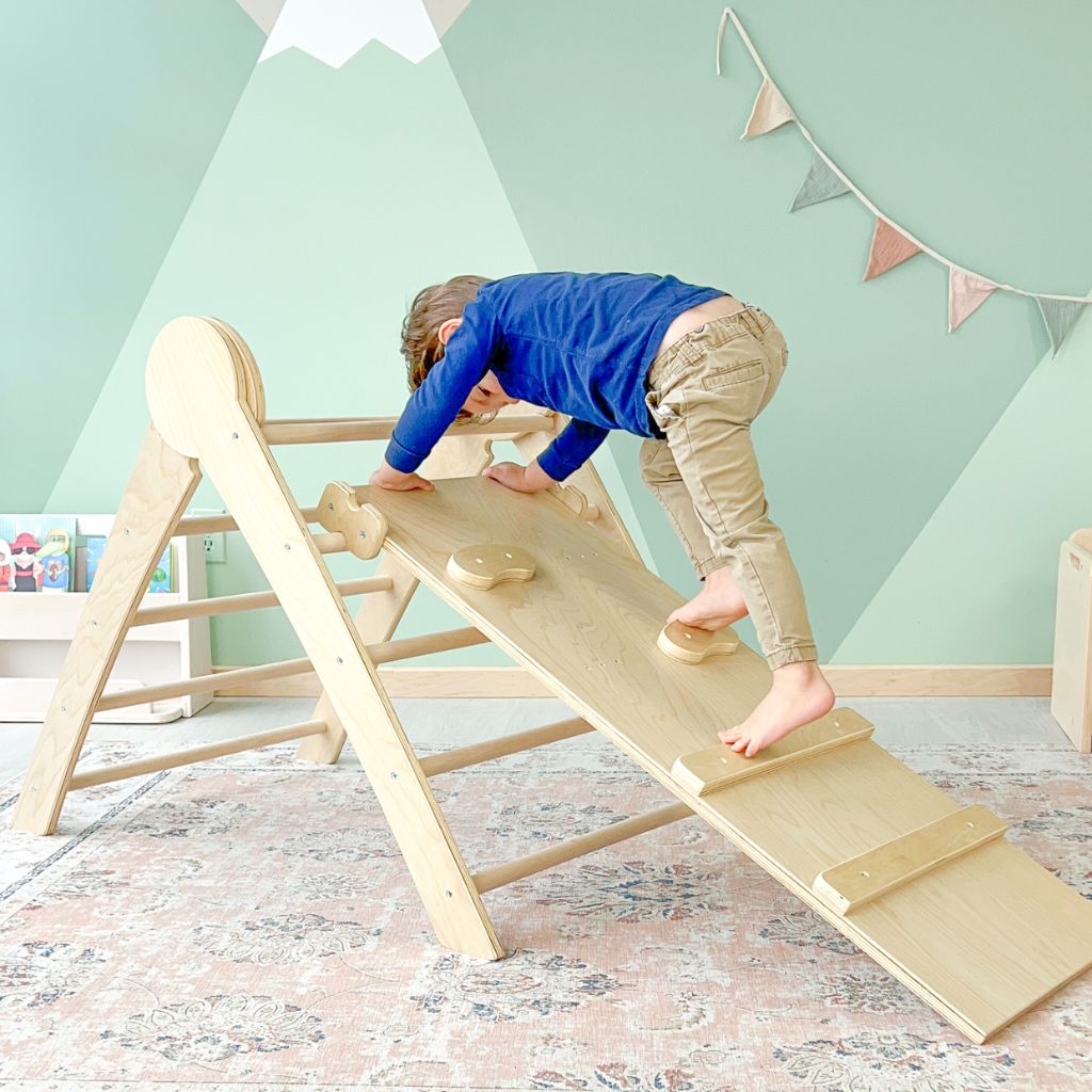 Toddler climbing through a wooden montessori climber using his foot to step on each peg or hold and wooden slat bar